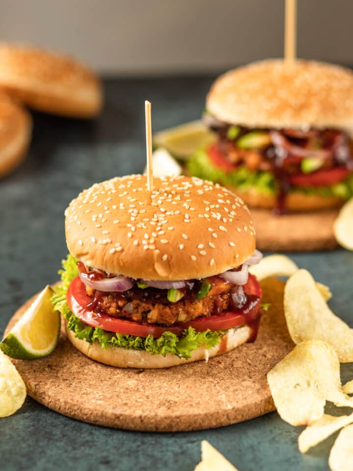 Shrimp burgers with lettuce, tomato, onions, and barbecue sauce. The burgers have sesame seed buns, and are set on cork plates.