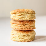 Three vegan biscuits stacked on top of one another. The biscuits are on top of a white counter.
