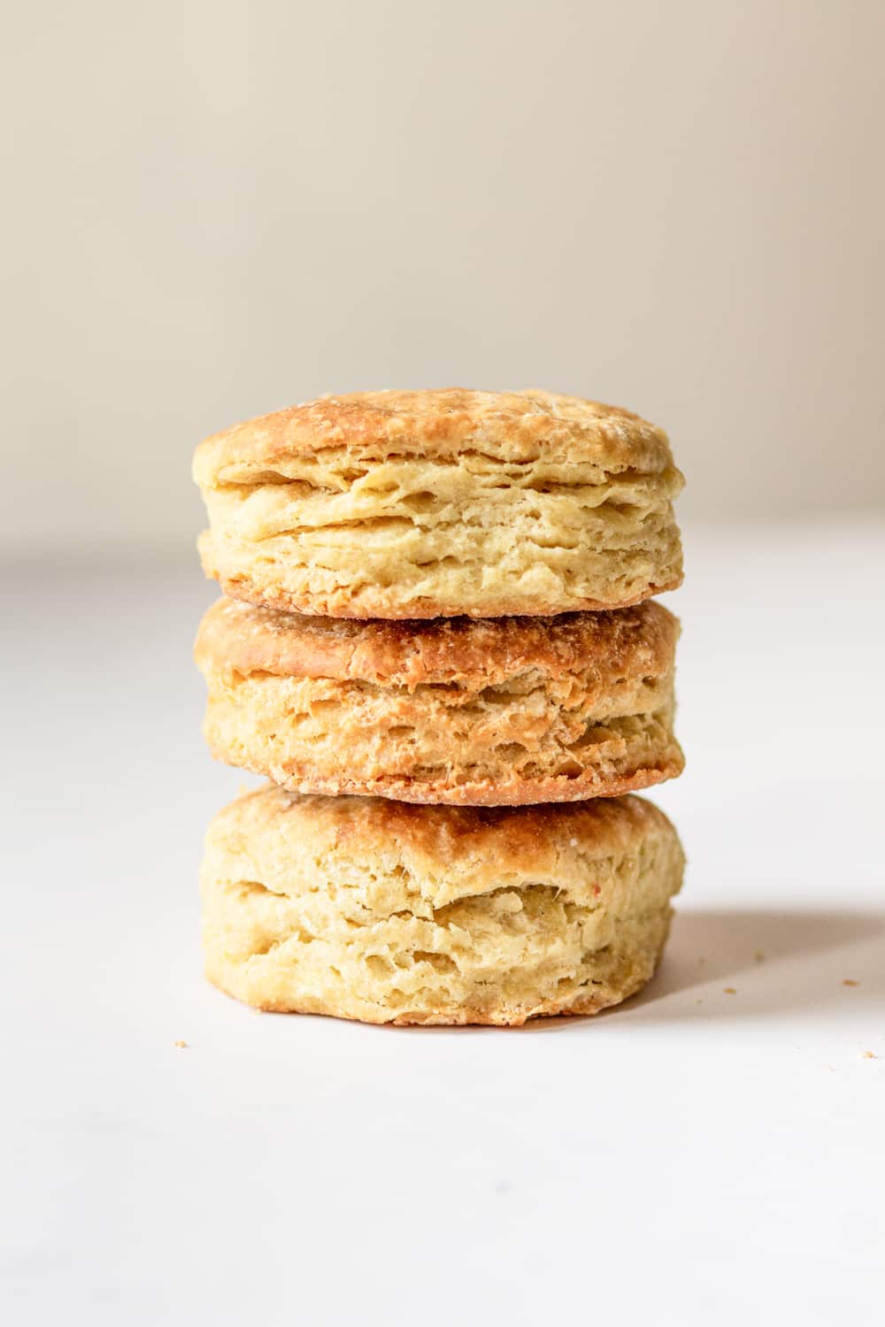 Three vegan biscuits stacked on top of one another. The biscuits are on top of a white counter.