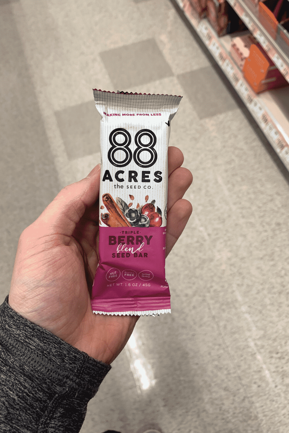 A hand holding a wrapped 88 Acres triple berry blend seed bar.