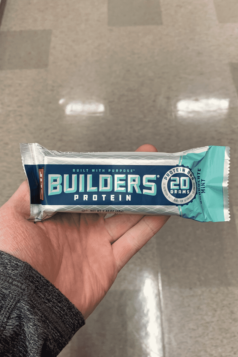 A hand holding a wrapped Clif builders bar mint chocolate flavored.