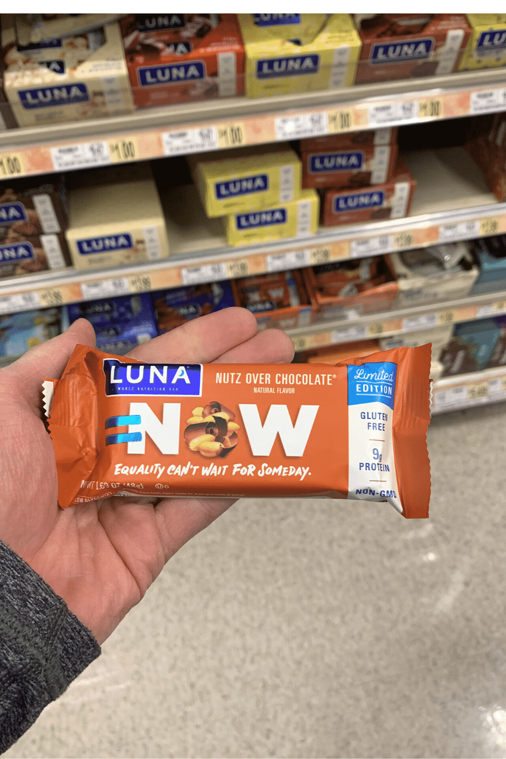 A hand holding a wrapped Luna nutz over chocolate flavored bar