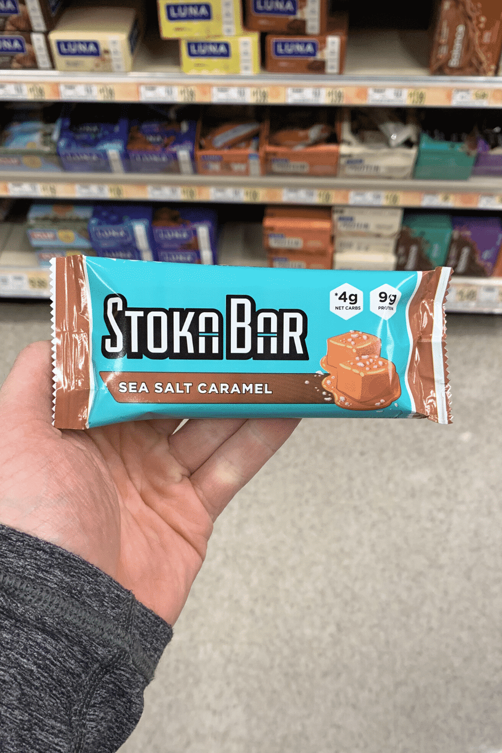 A hand holding a wrapped sea salt caramel flavored Stoka bar