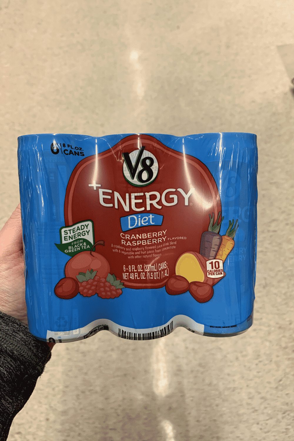 A hand holding a six pack of V8 diet energy cranberry raspberry flavored.