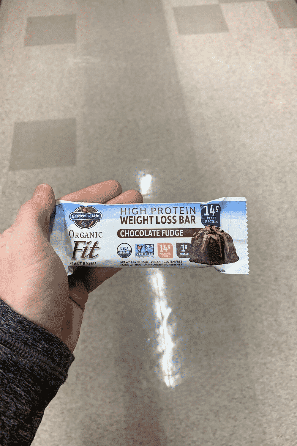 A hand holding a wrapped chocolate fudge garden of life high protein fat loss bar