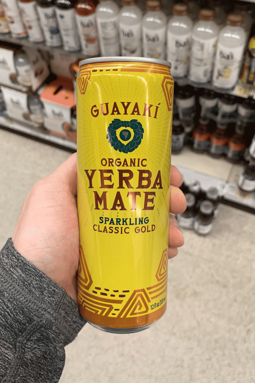 A hand holding a can of Guyaki organic yerba mate sparkling classic gold