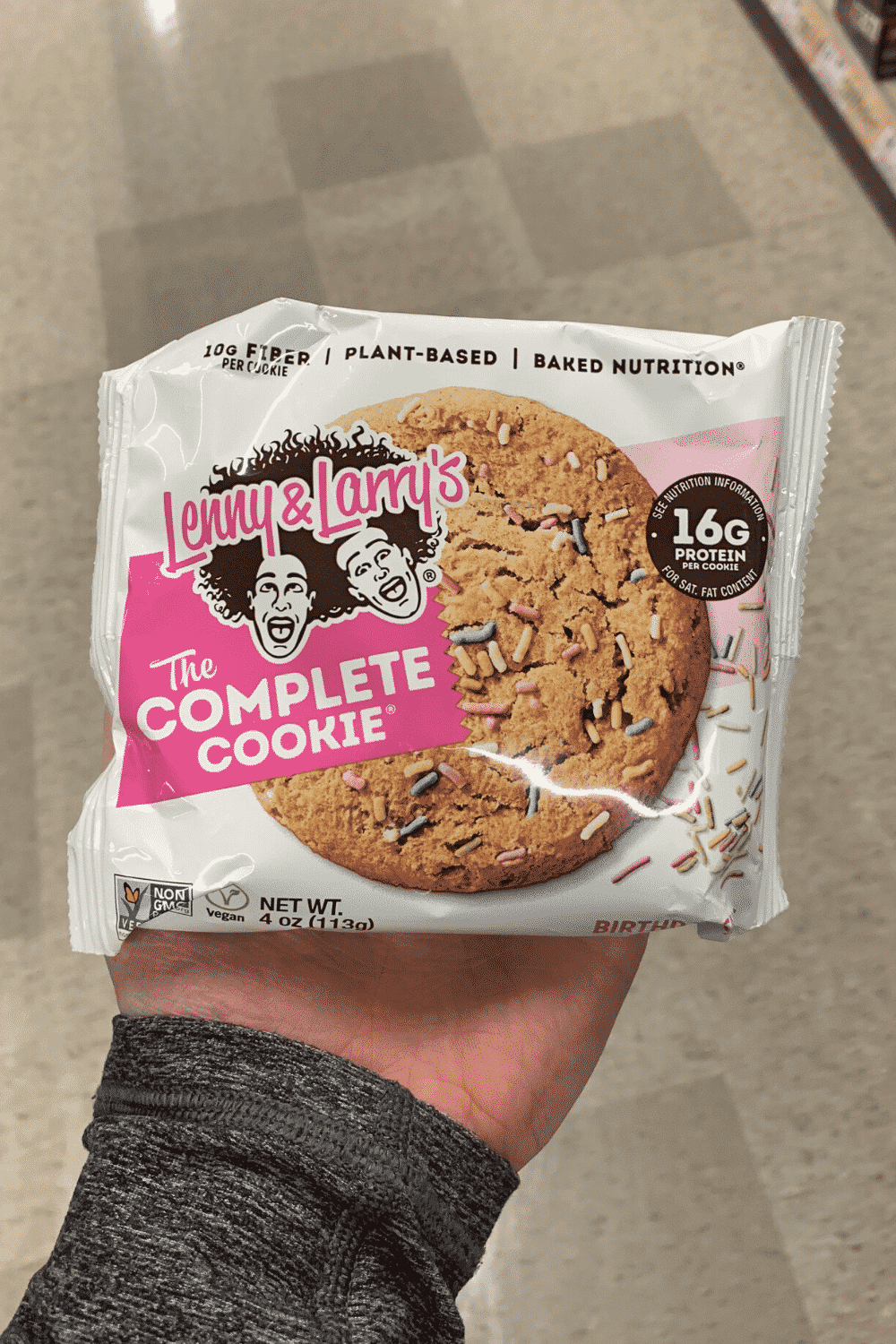 A hand holding a wrapped Lenny and Larry's Complete Cookie birthday cake flavor.