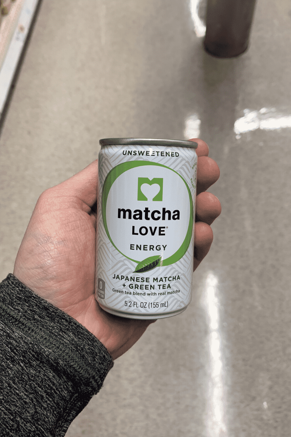 A hand holding a can of unsweetened matcha love energy.