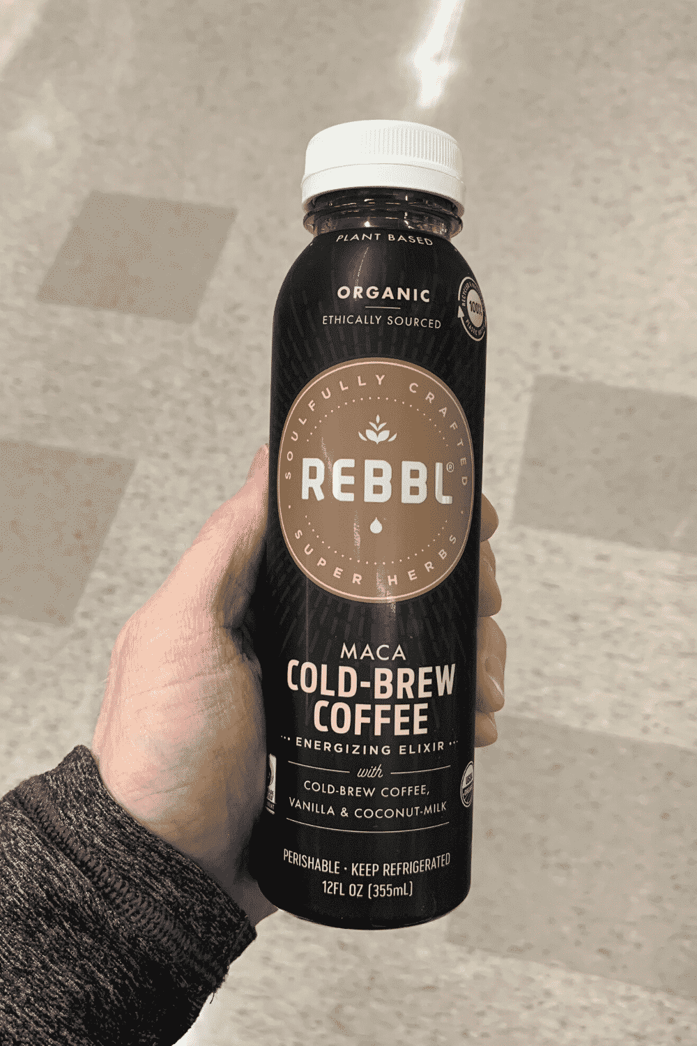 A hand holding a bottle of Rebbl maca cold-brew coffee