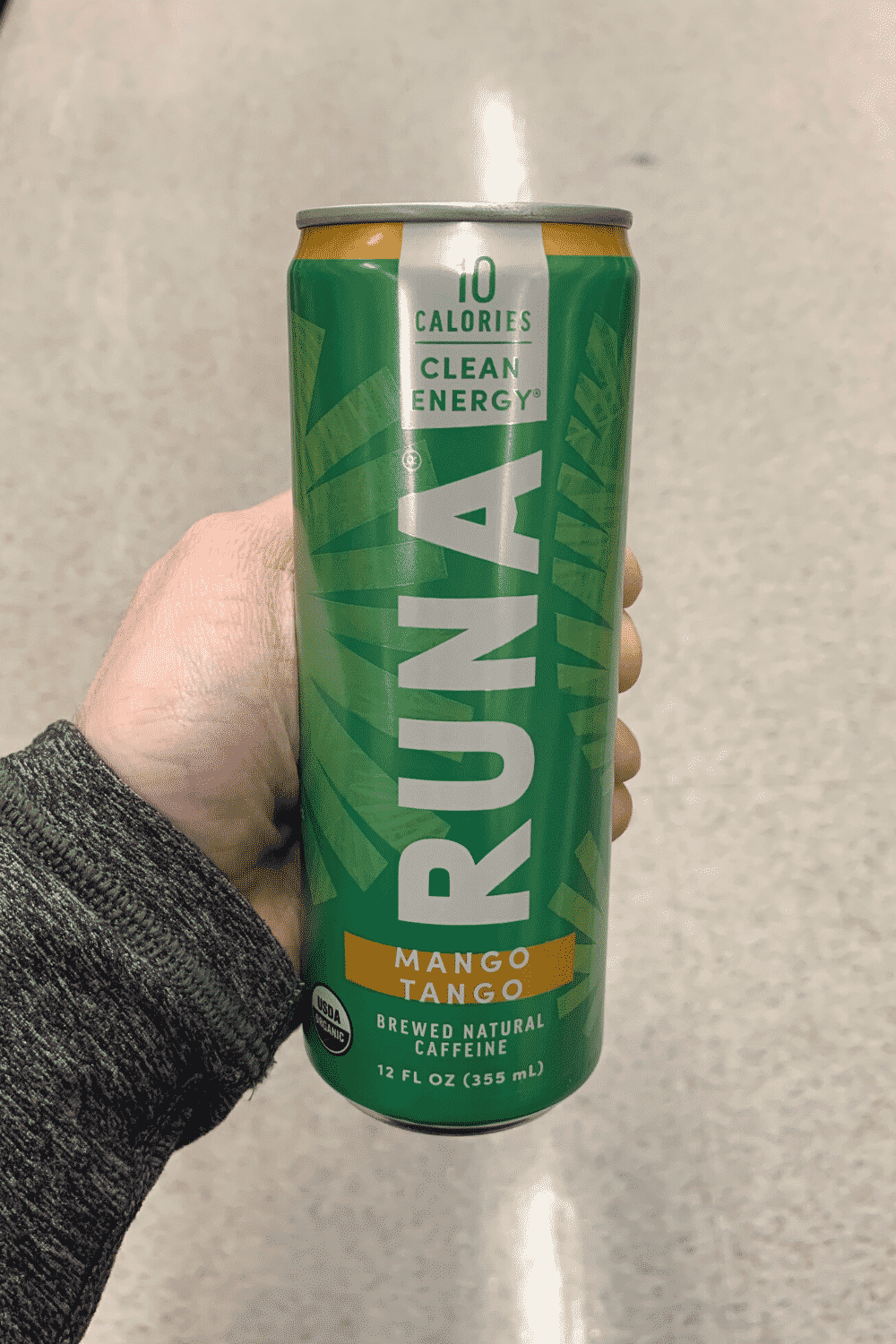 A hand holding a can of Runa mango tango falvor