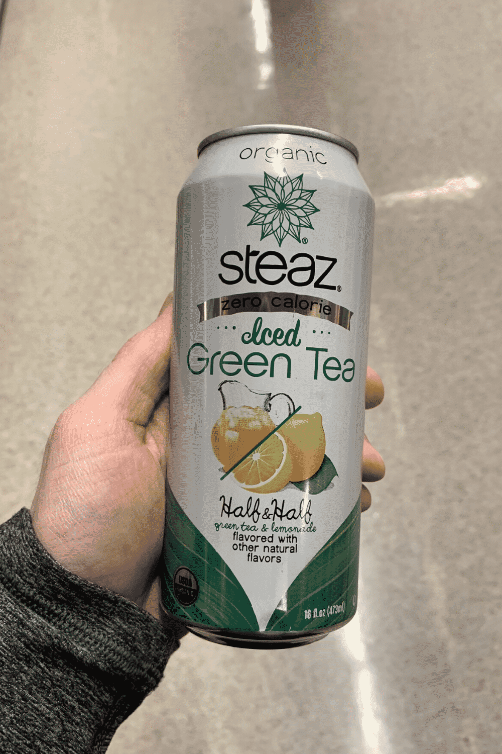 A hand holding a can of zero calories Steaz iced green tea