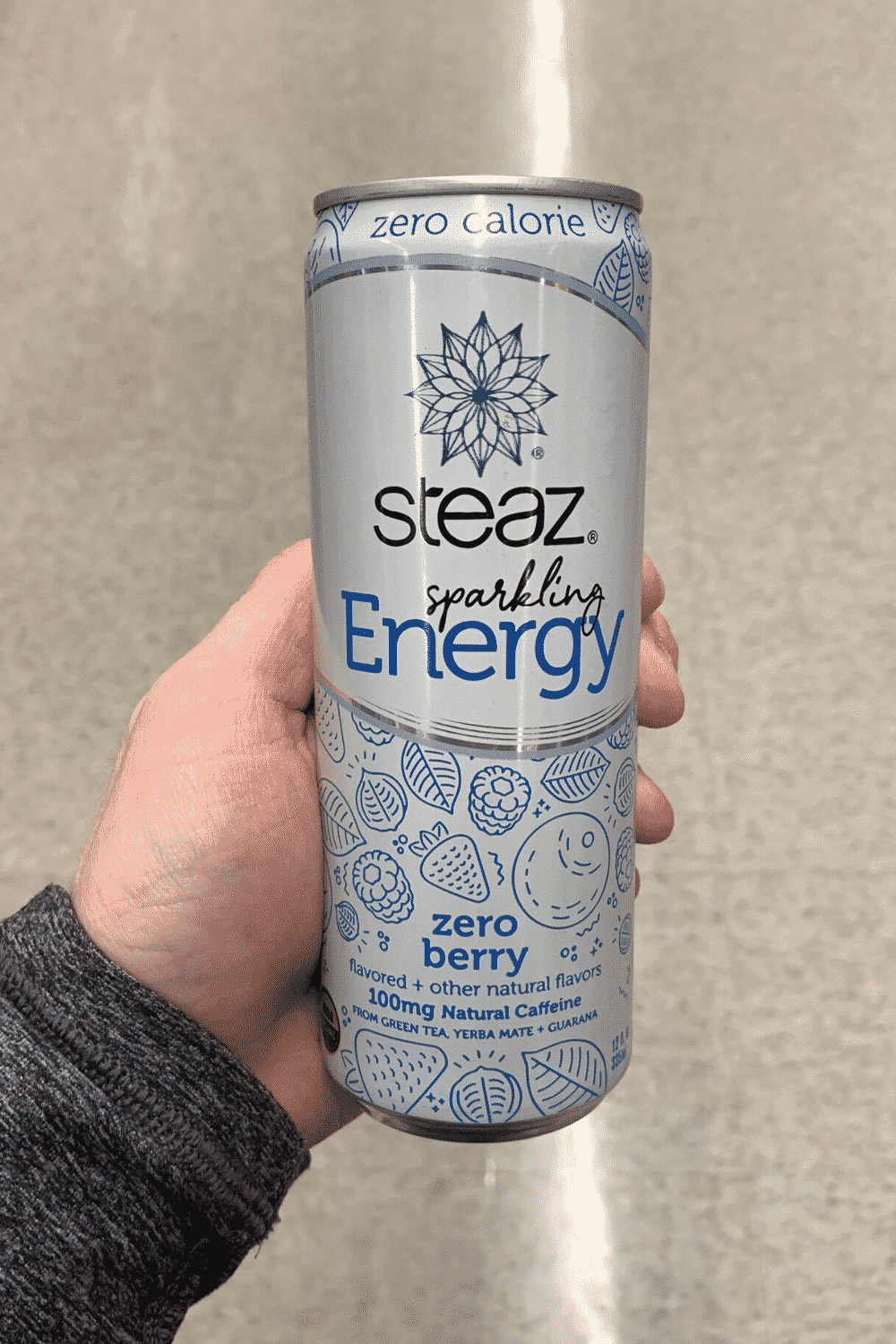 A hand holding a can of zero calorie zero berry flavored Steaz sparkling energy drink
