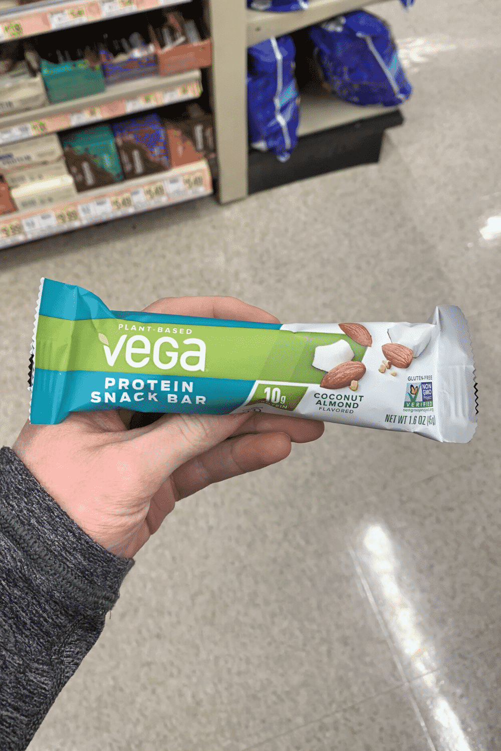 A hand holding a wrapped vega protein snack bar coconut almond flavored.