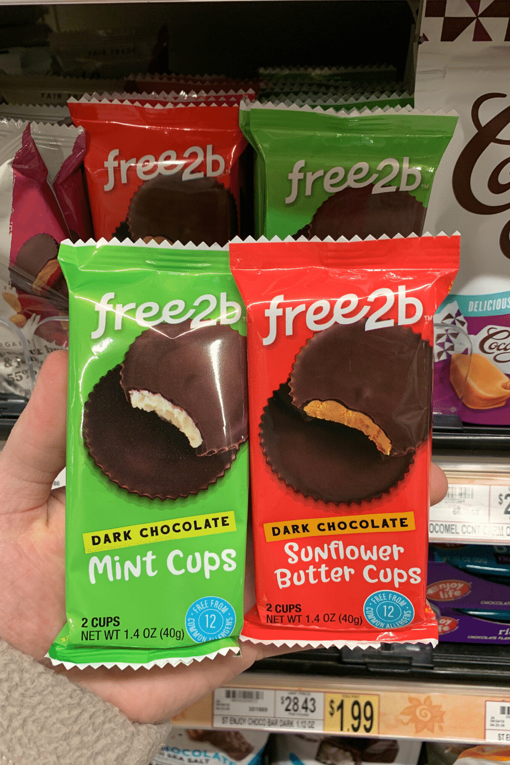 A hand holding one package of free2b mint cups and one package of sunflower butter cups