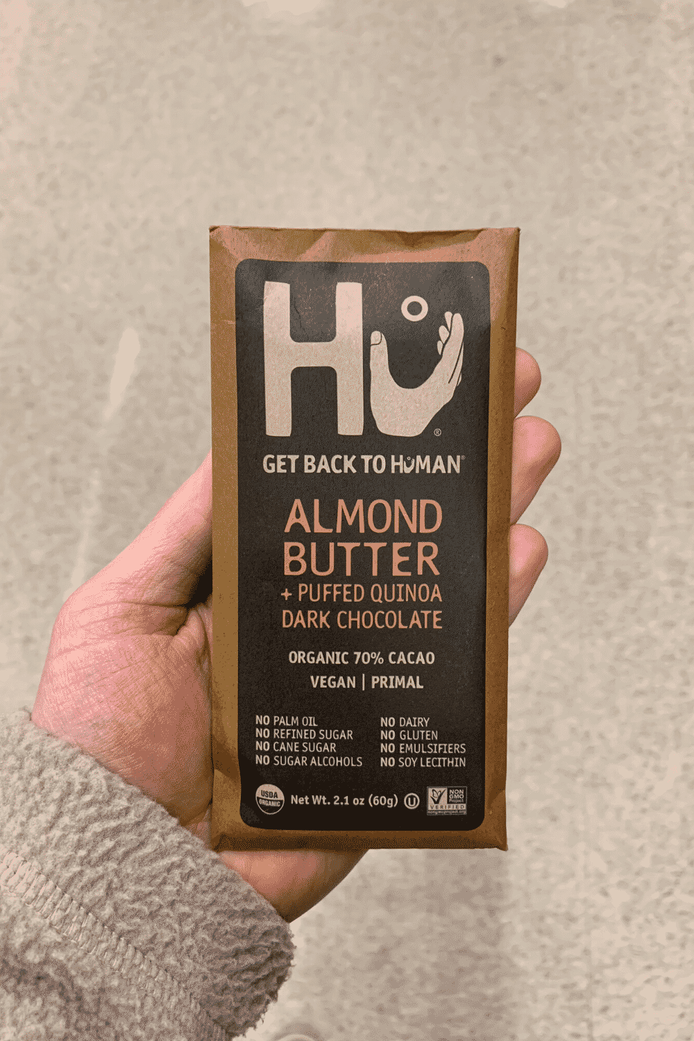 A hand holding a Hu vegan chocolate bar Almond Butter and Puffed Quinoa Dark Chocolate