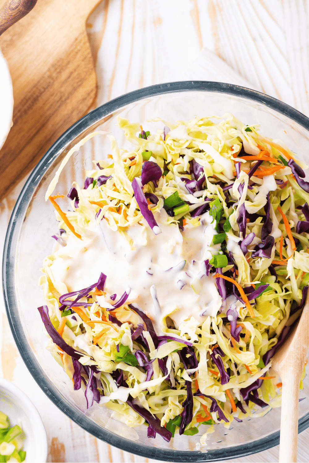 A glass bowl filled with keto coleslaw with keto coleslaw dressing on top.