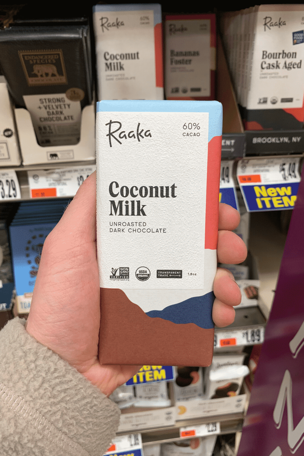 A hand holding a Raaka coconut milk unroasted dark chocolate bar