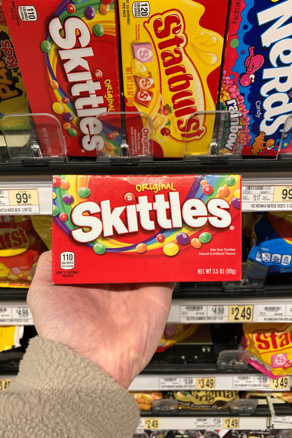 A hand holding a pack of skittles