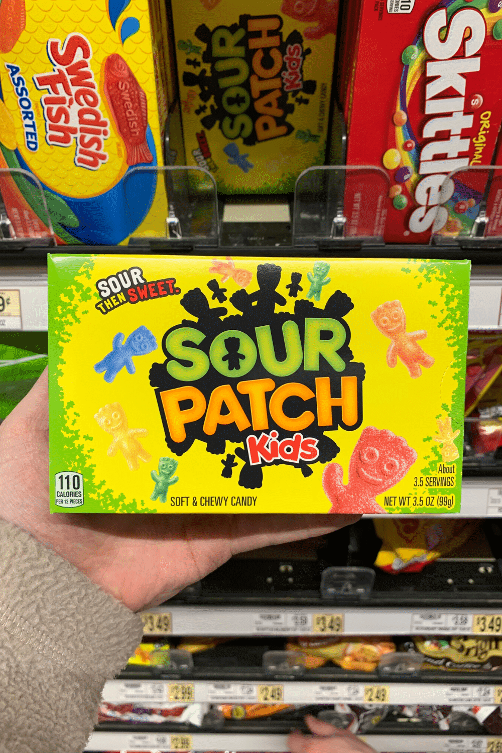 A hand holding a pack of sour patch kids