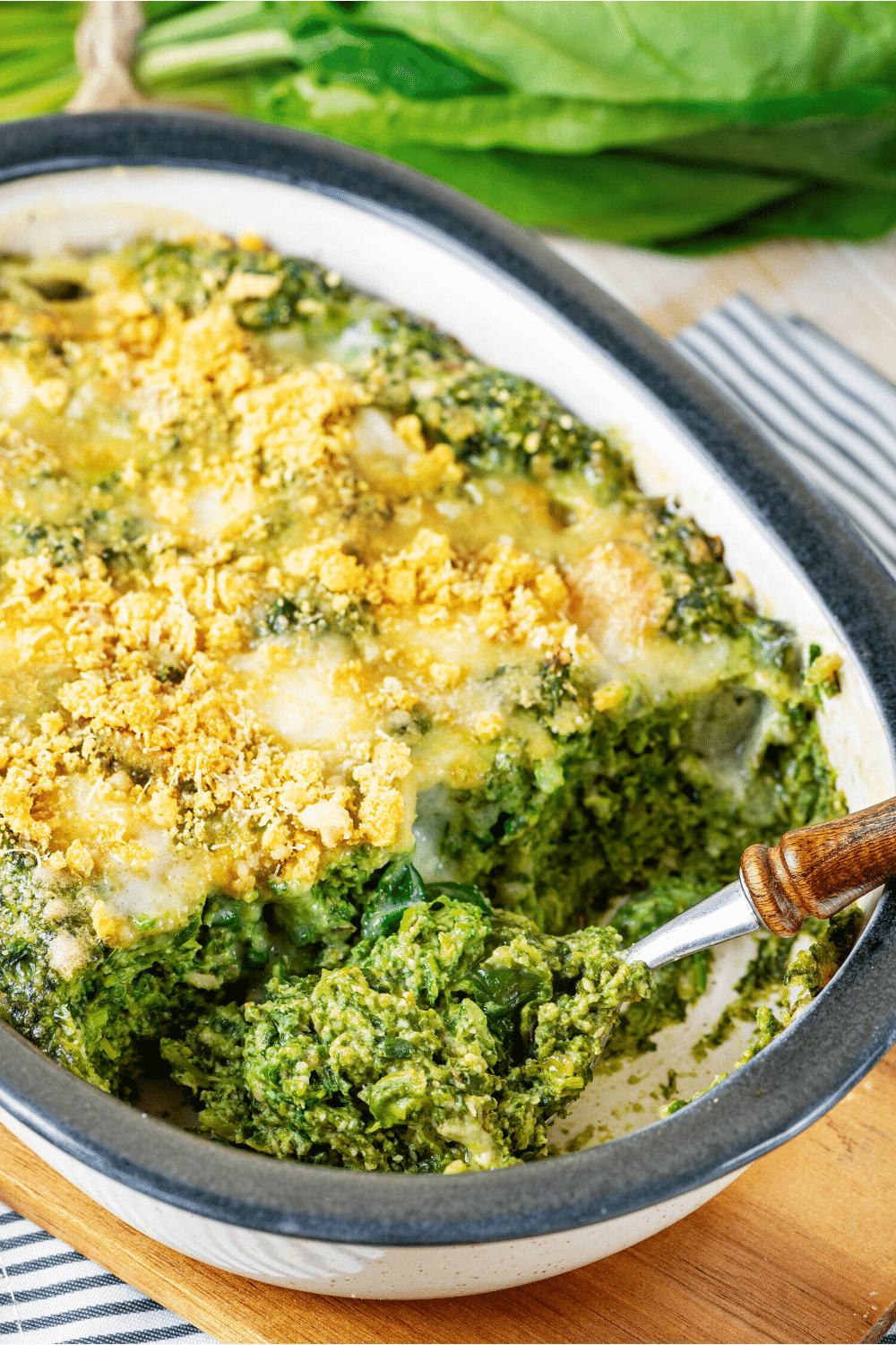 Spinach casserole in a baking dish. There is a spoon at the front of the dish with a scoop of the spinach casserole on it.