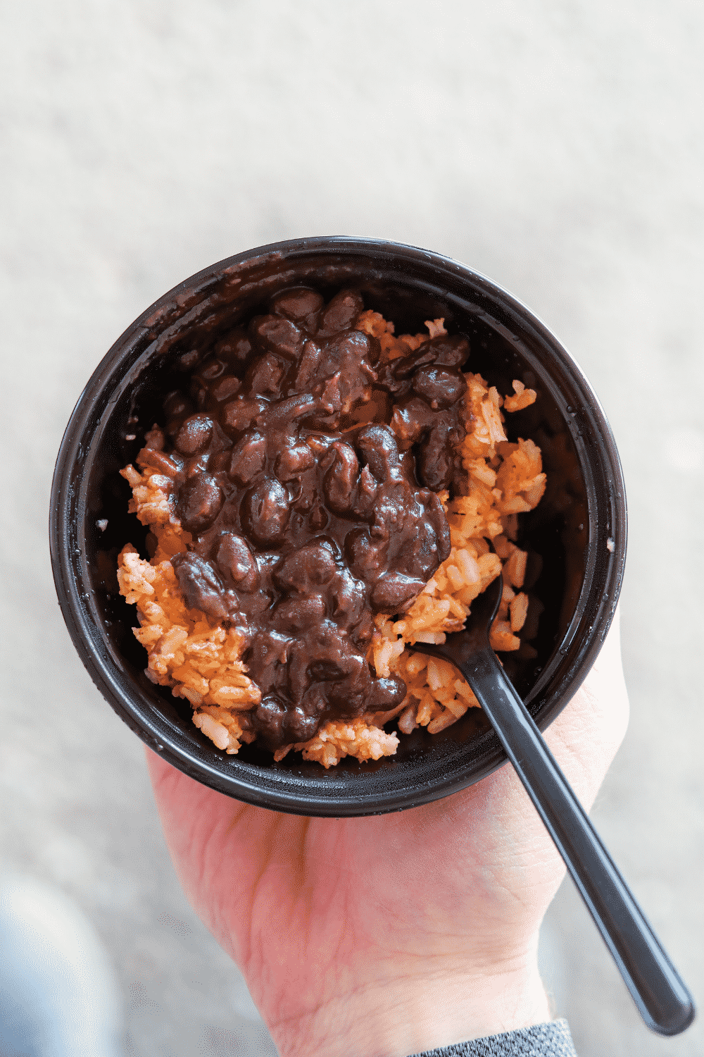 A hand holding a bowl of Taco Bell black beans and rice