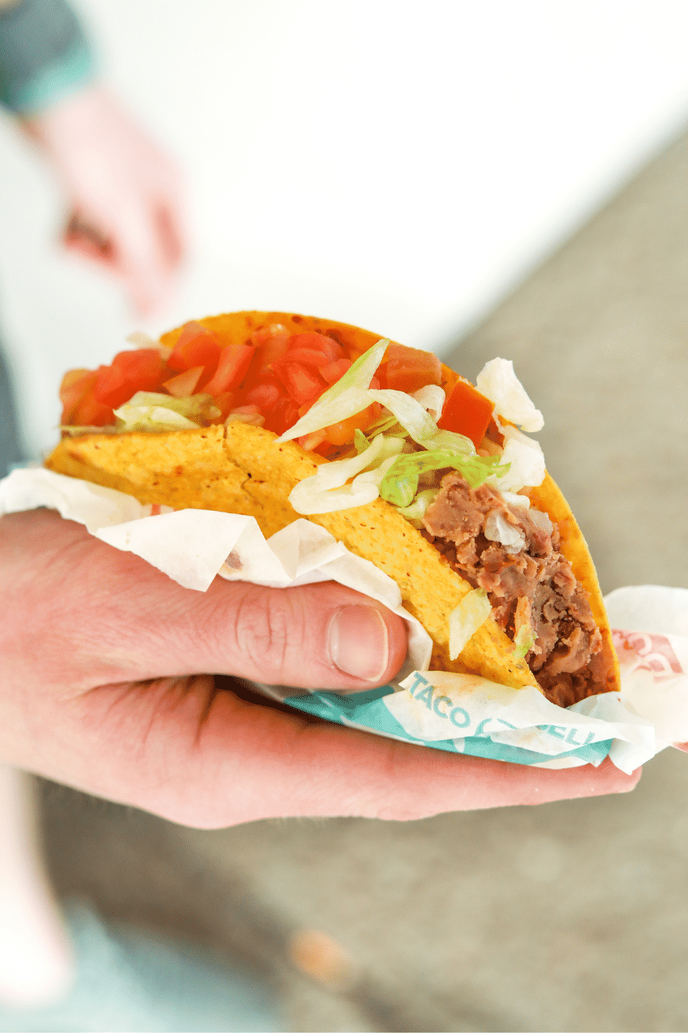 A hand holding a Taco Bell vegan crunchy taco