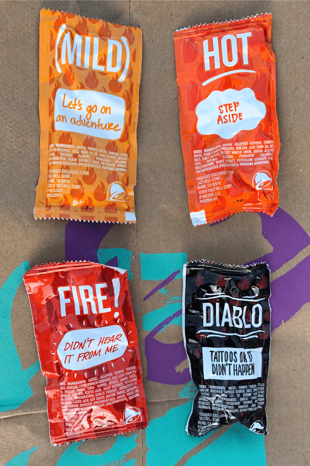 A mild, hot, fire, and diablo Taco Bell sauce packets on a brown Taco Bell bag.