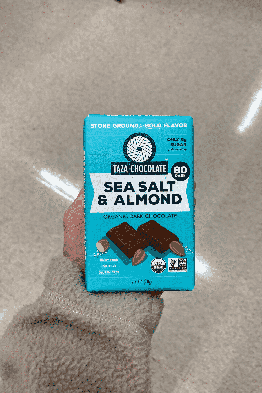 A hand holding a Taza Chocolate Sea Salt and Almond organic vegan dark chocolate bar.