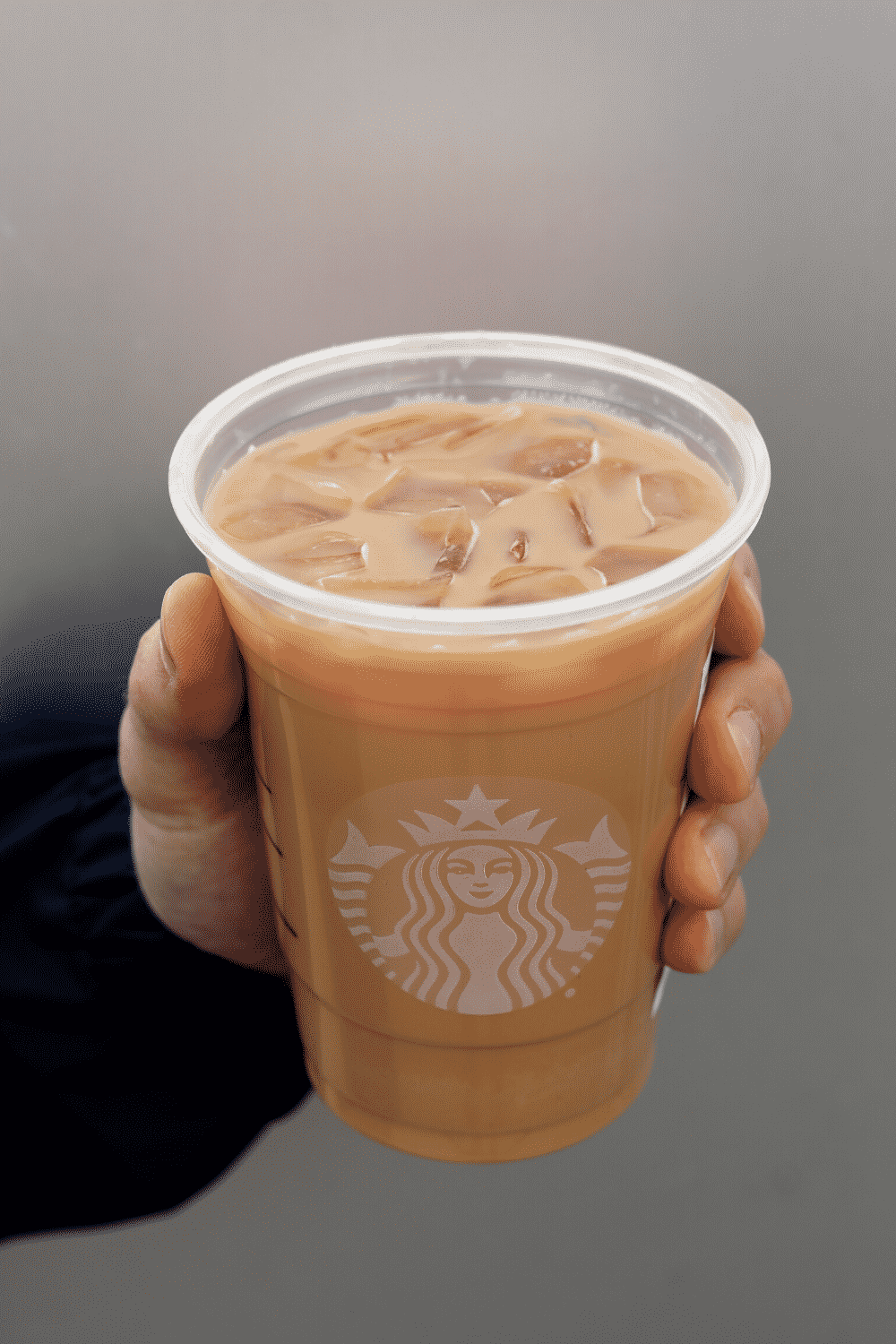 A hand holding a cup of Starbucks vegan iced Caffe latte