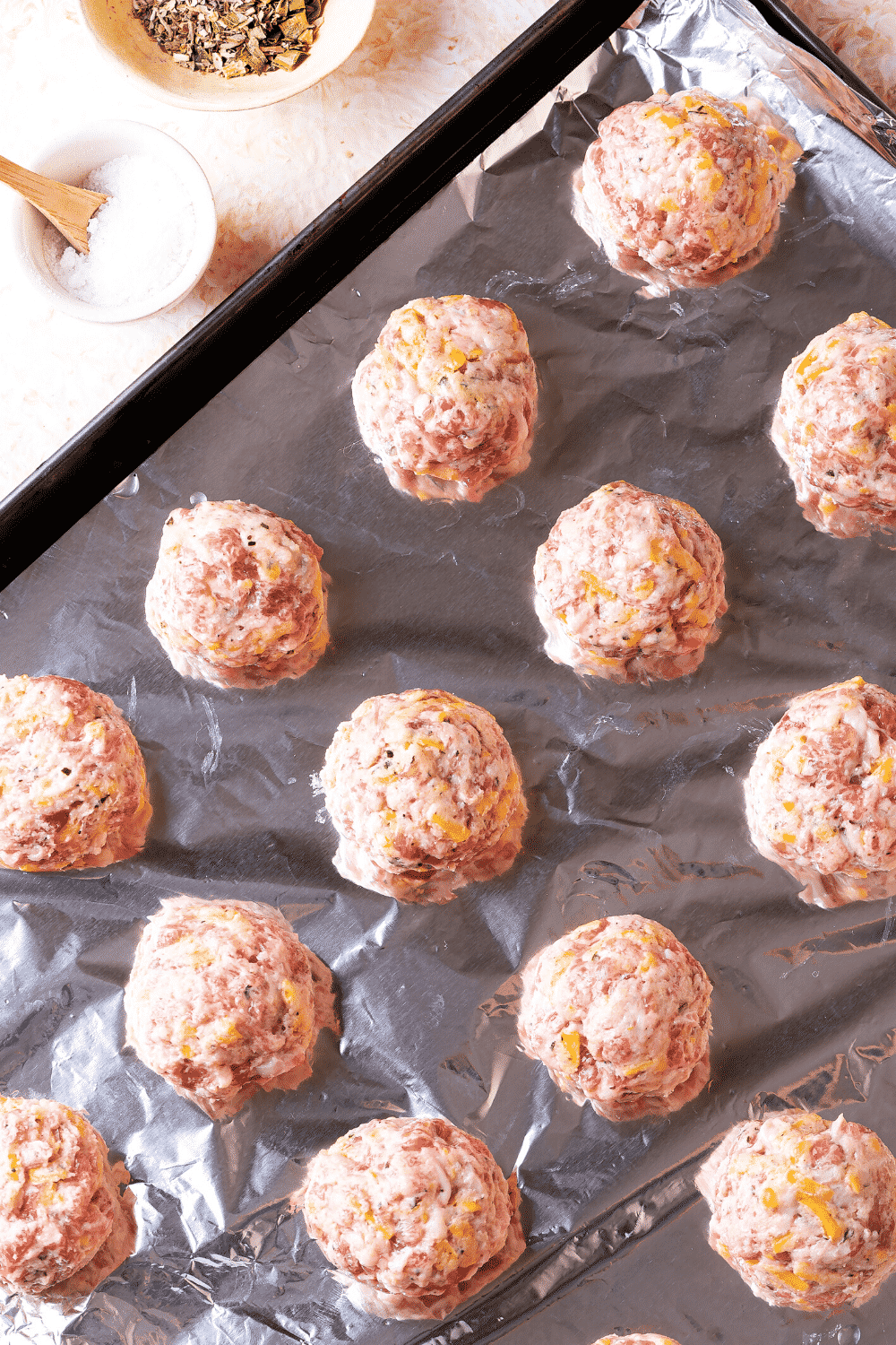 Three rows on uncooked keto sausage balls on tin foil on a baking sheet.