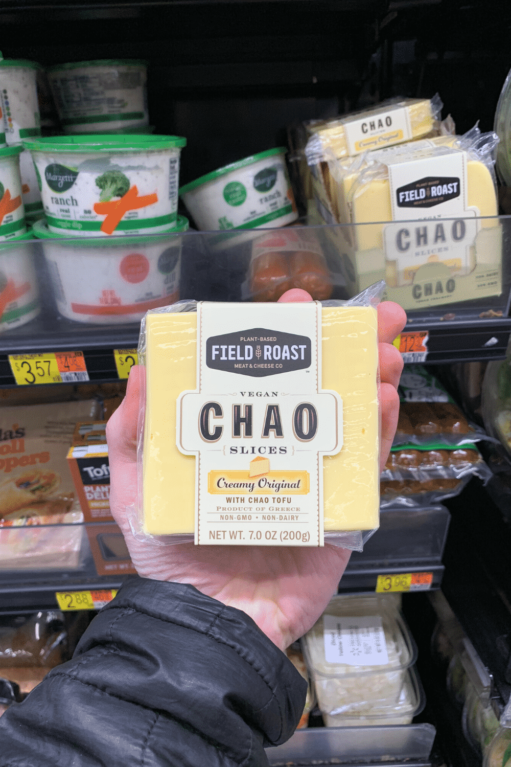A hand holding plant-based field roast vegan chao slices creamy original with chao tofu.