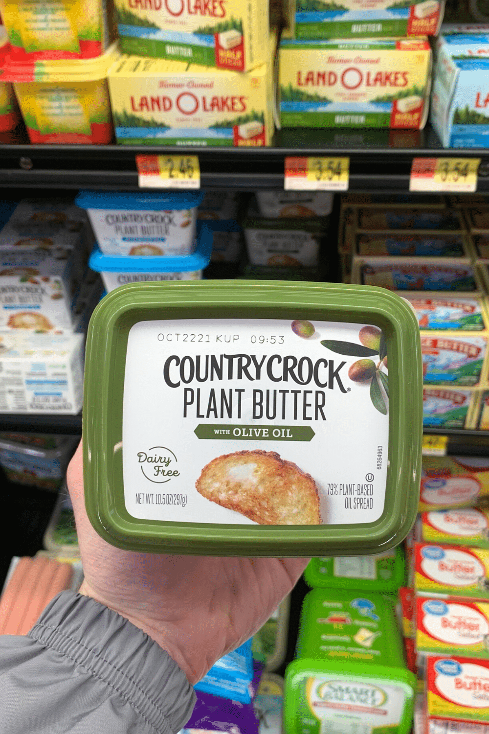 A hand holding Country crock plant butter with olive oil.