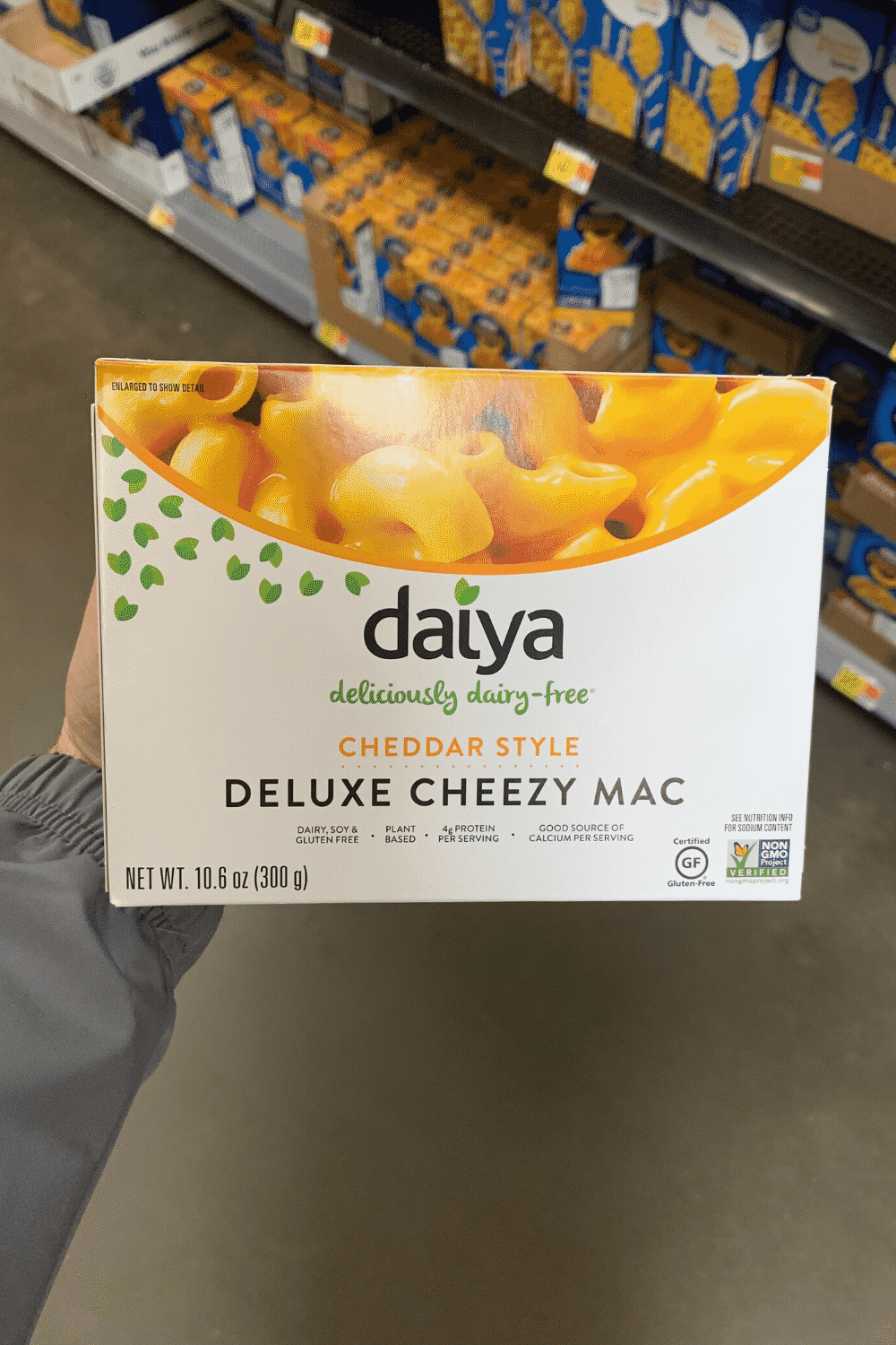 A hand holding Daya cheddar style deluxe cheesy Mac.