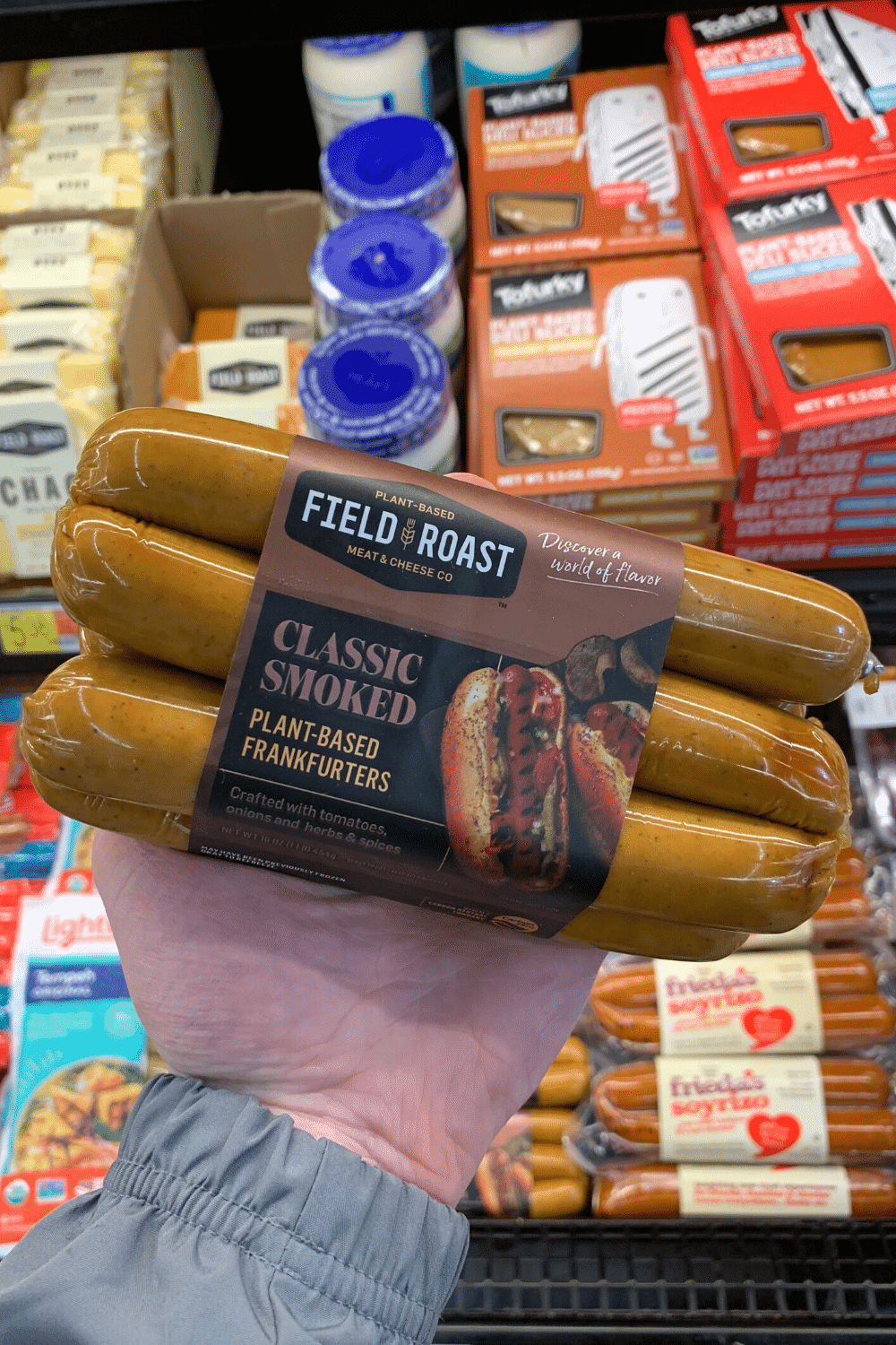 A hand holding field roast plant-based Classix smoked smoke frankfurters.