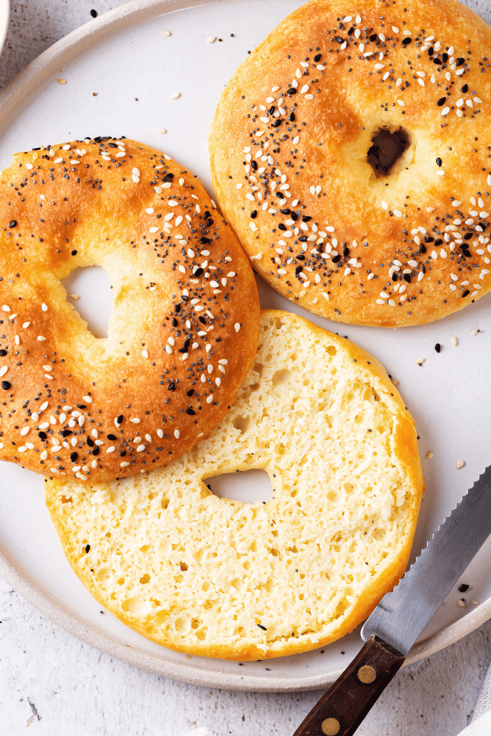 A white plate with two bagels on it. One bagel is cut in half with the bottom side facing up and top side facing down.