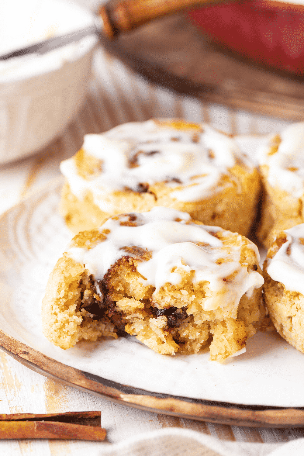 A white plate with a cinnamon roll with a bite out of it and a whole cinnamon roll behind it..