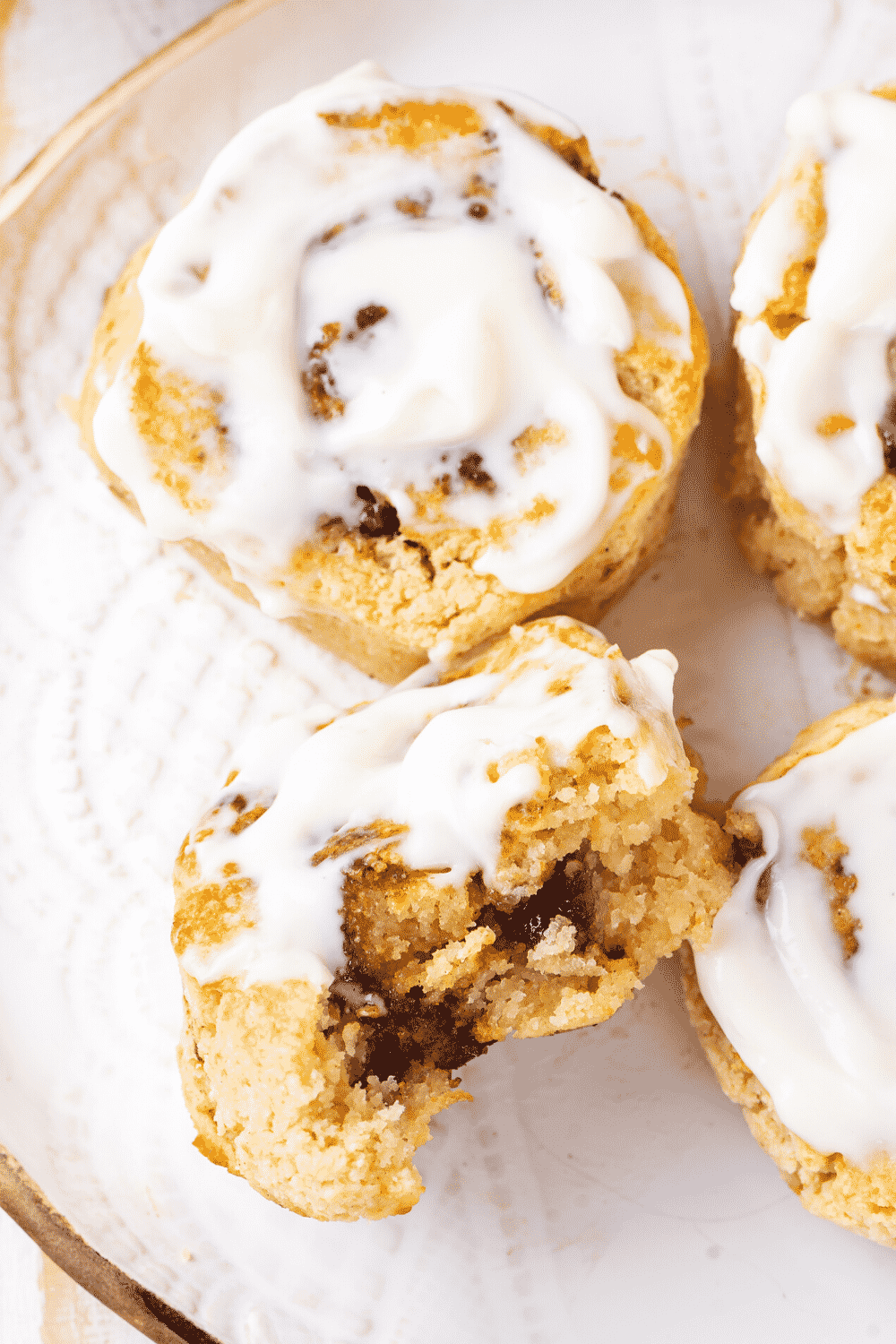 A white plate with one cinnamon roll and another cinnamon roll in front of it on its side with a bite out of it.