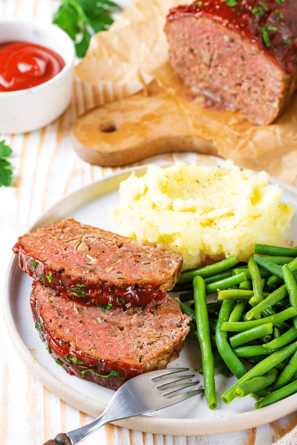 A white plate with two slices of meatloaf mashed potatoes and green beans on it.