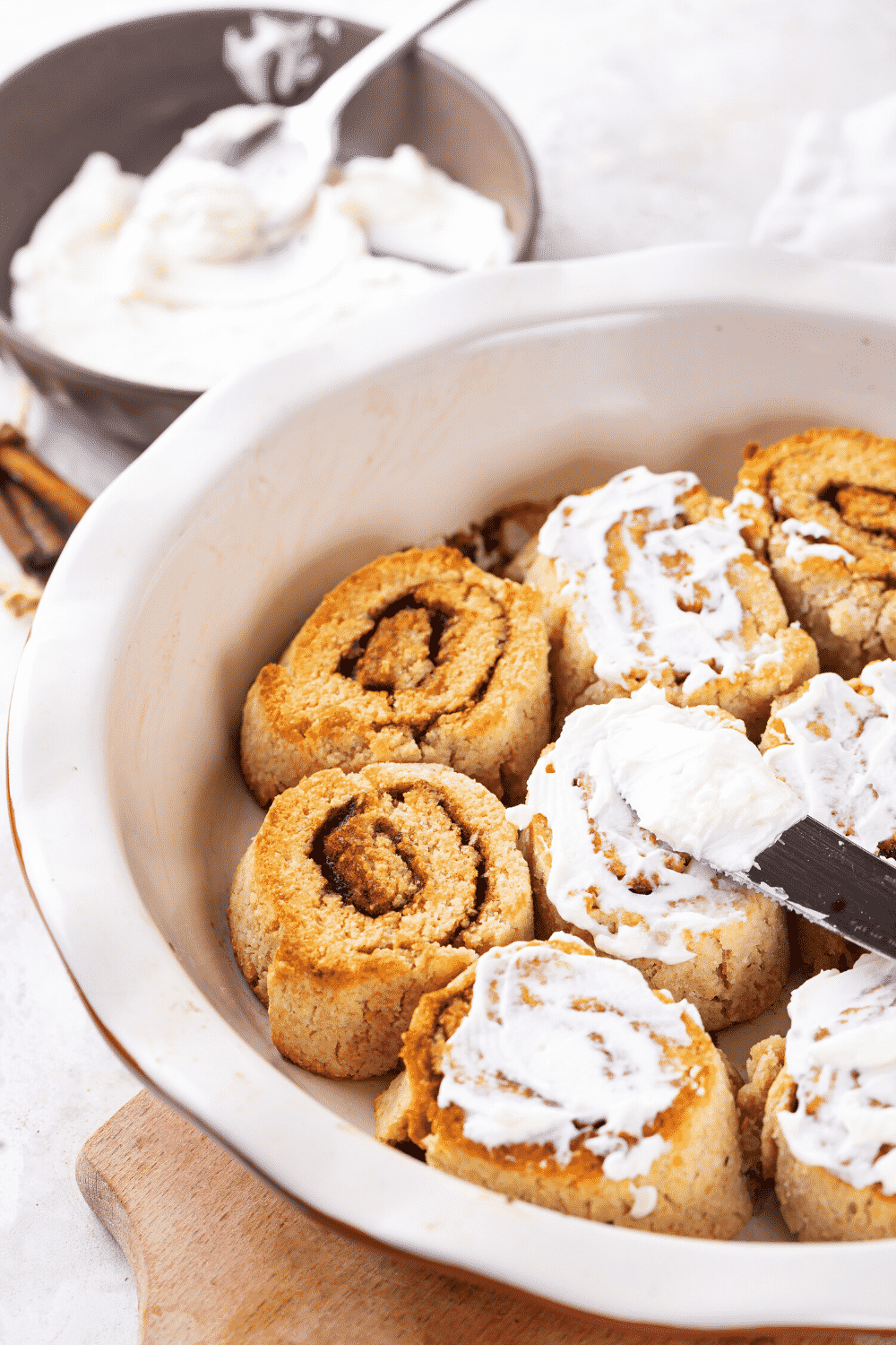 A white baking dish filled with two cinnamon rolls, three cinnamon rolls with icing on them, and then three more cinnamon rolls to the right of those.