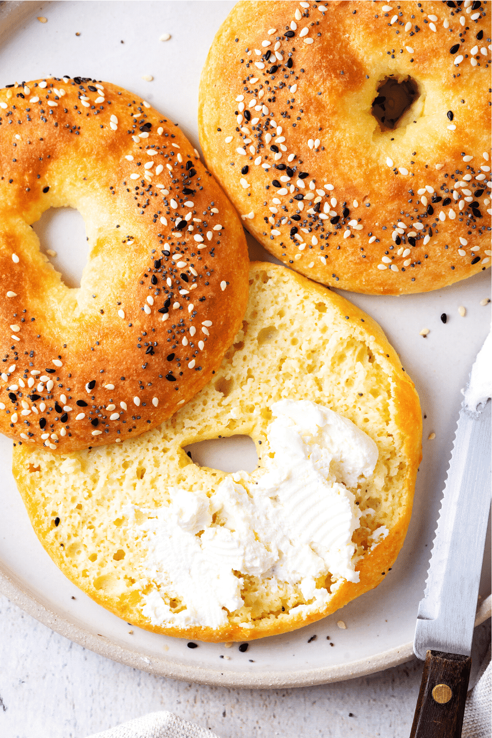 A white plate with a whole bagel and sliced bagel on it. The sliced bagel has some butter spread on the bottom half.