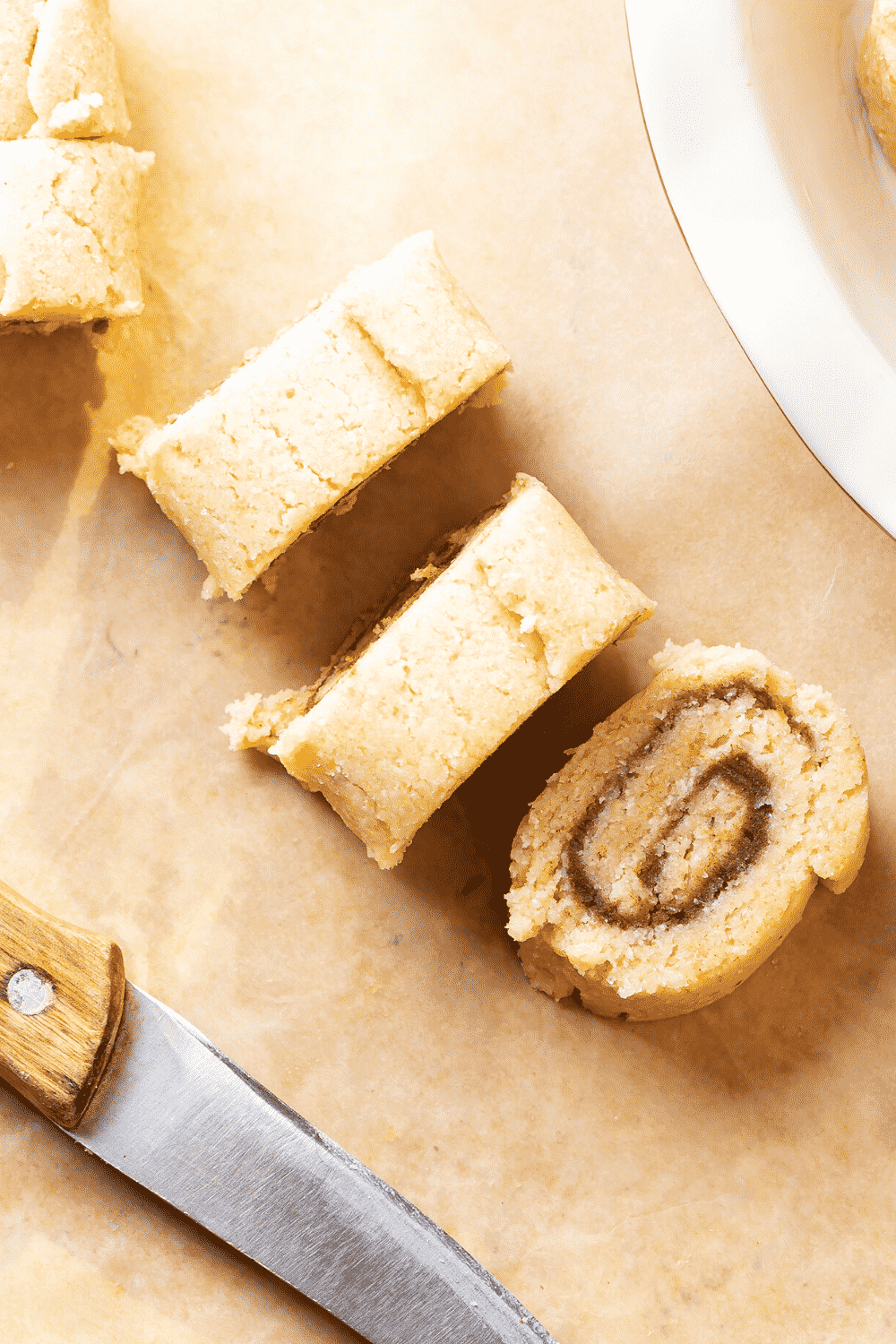 Cinnamon roll doll cut into three rolls on a piece of parchment paper.