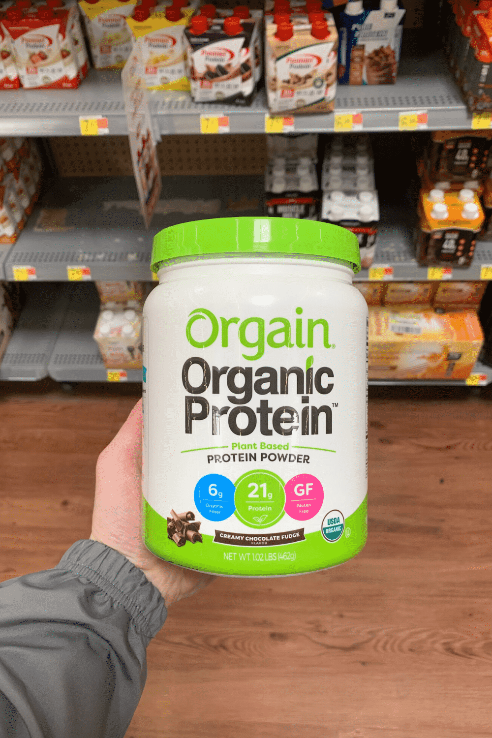 A hand holding Orgain organic creamy chocolate fudge plant-based protein powder.