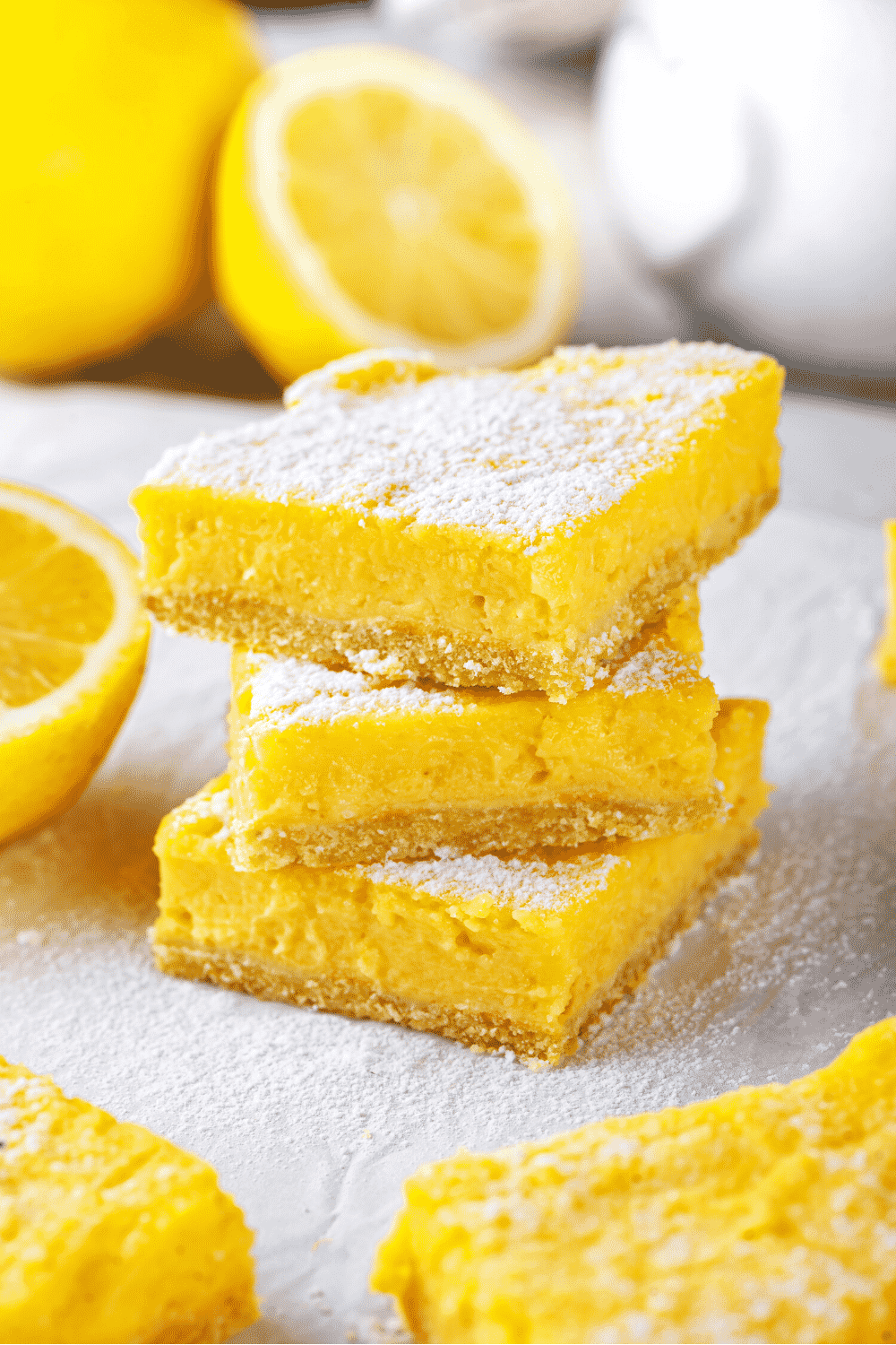 A stack of three keto lemon bars. The white counter the lemon bars are on is covered in powdered sugar.