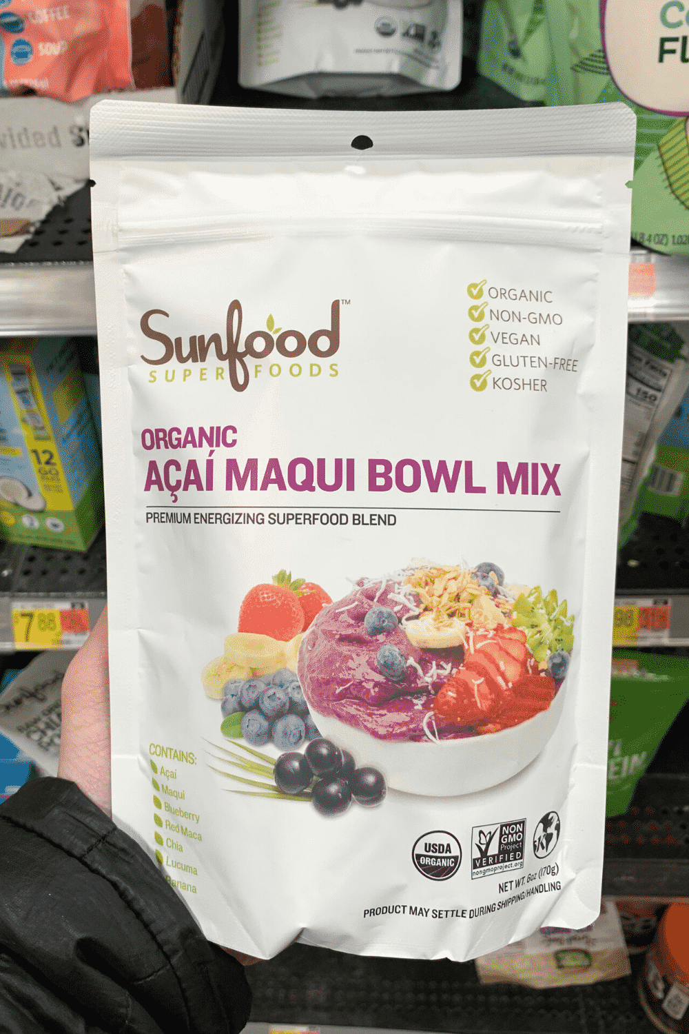 A hand holding sun food super foods organic acai maqui bowl mix.