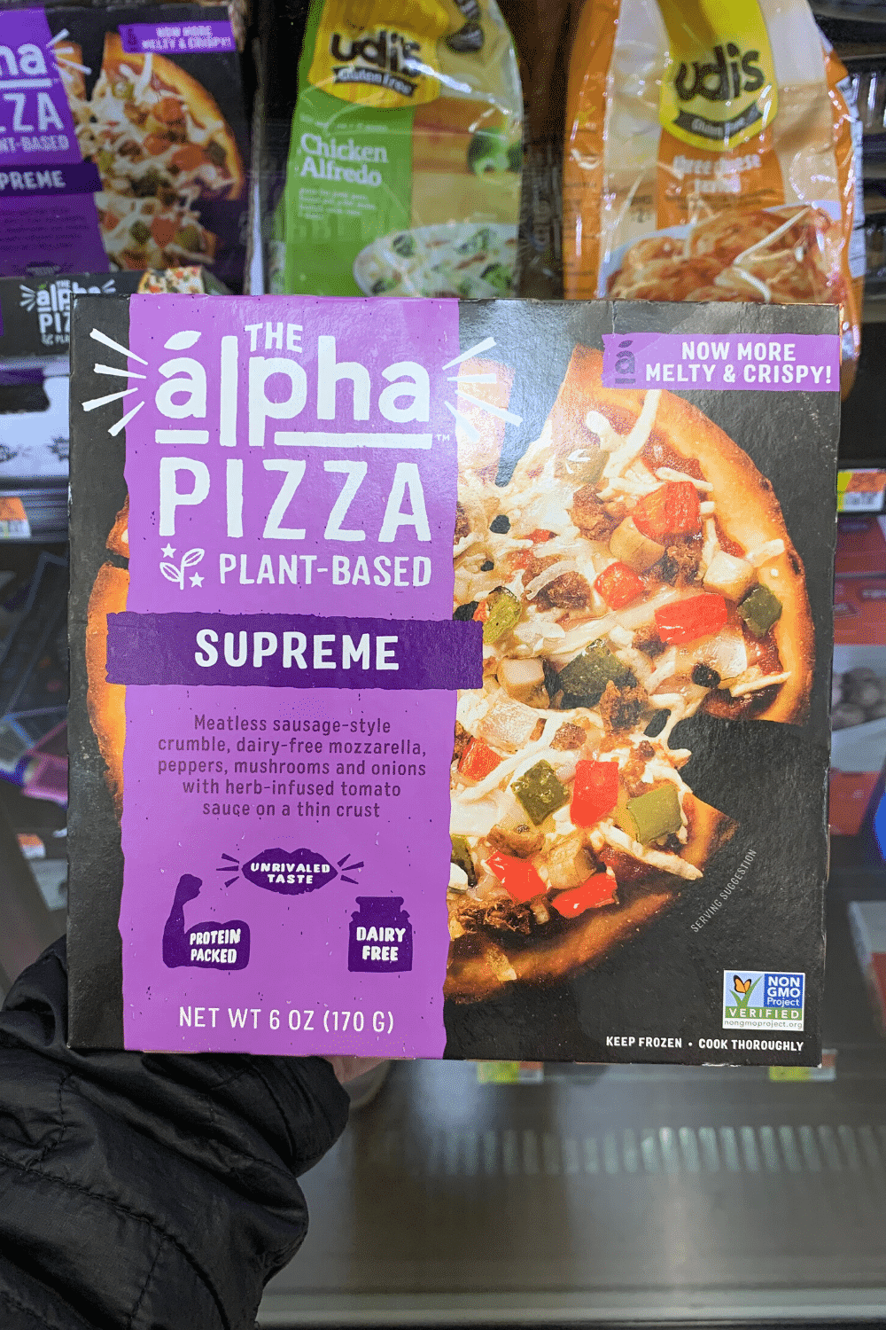 A hand holding the alpha pizza plant-based supreme.