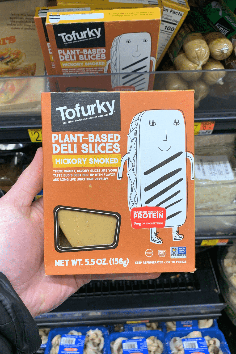 A hand holding Tofurkey Plant based deli slices hickory smoked flavor.