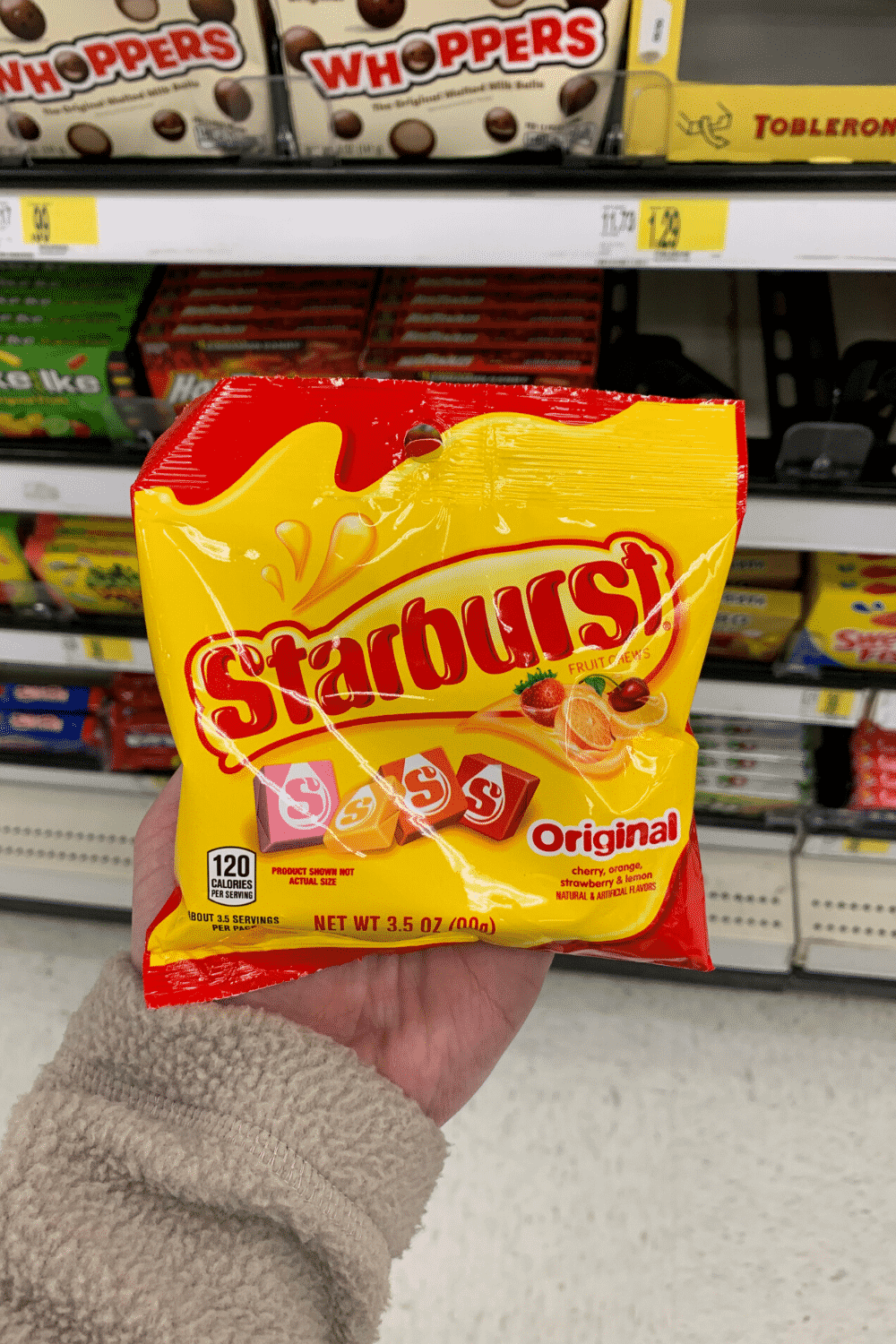 A hand holding a bag of Starburst candy.