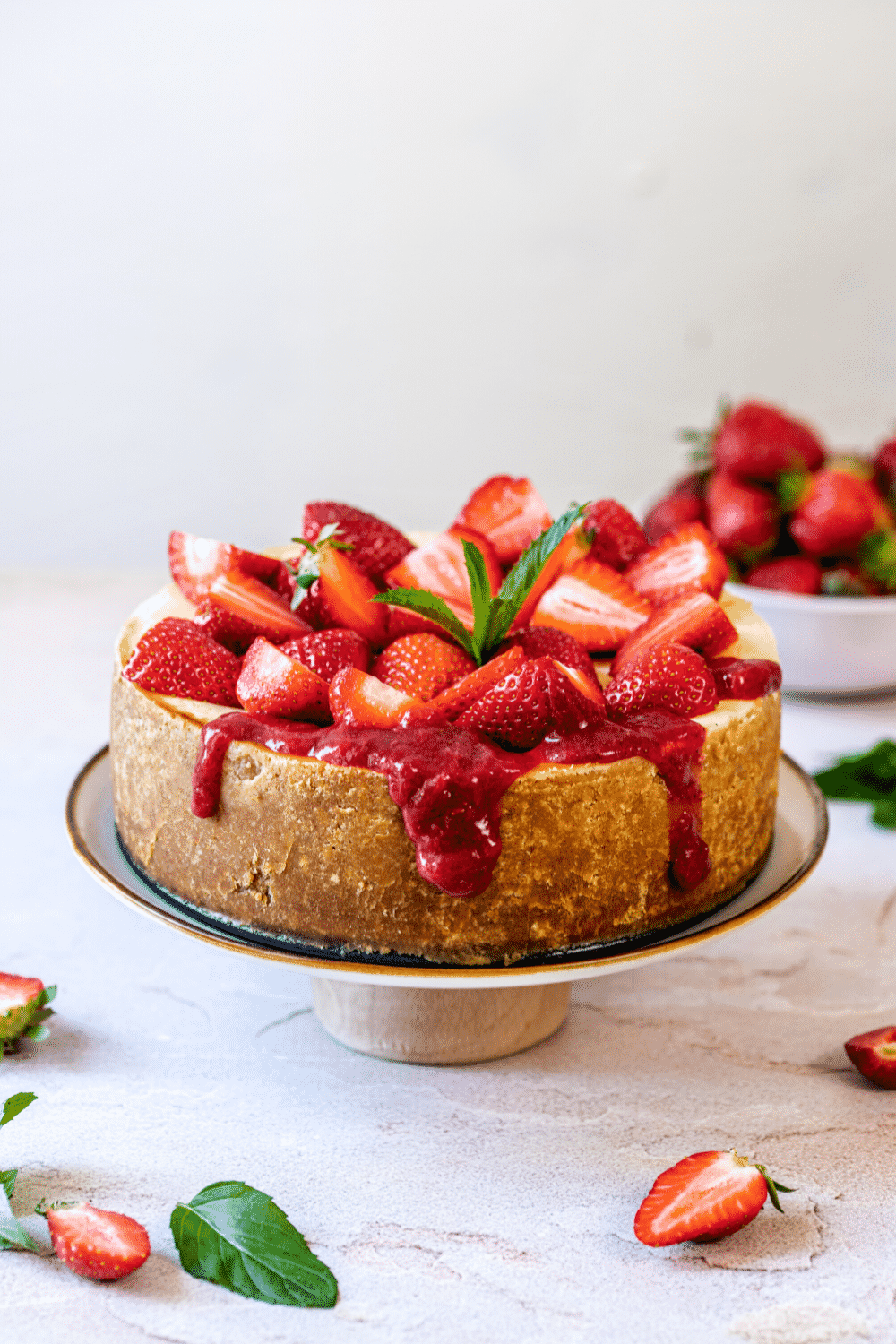 A whole strawberry cheesecake topped with fresh strawberries and strawberry sauce. The cheesecake is on a serving dish on a white counter.