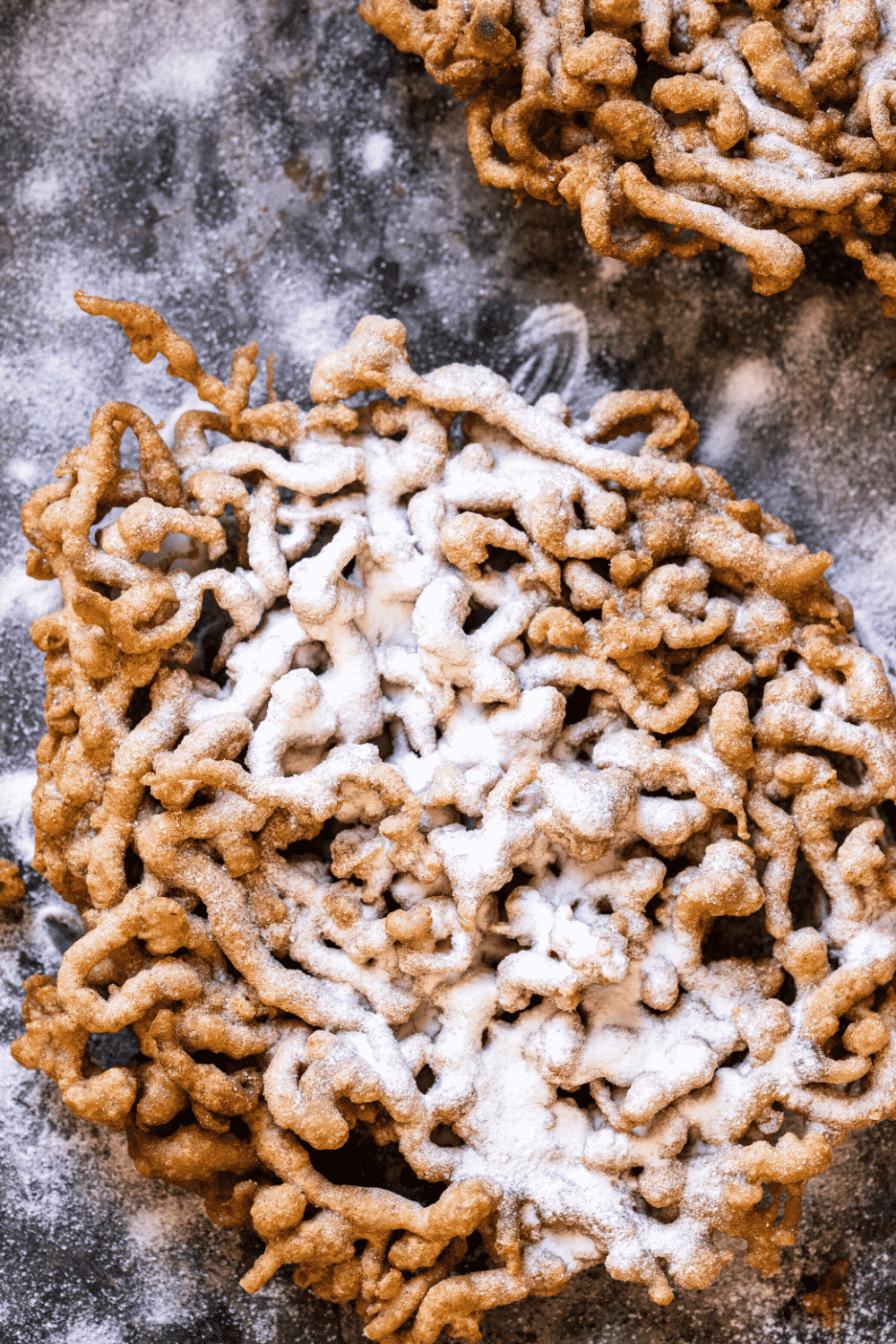 A funnel cake on black table. The table is covered in powdered sugar.