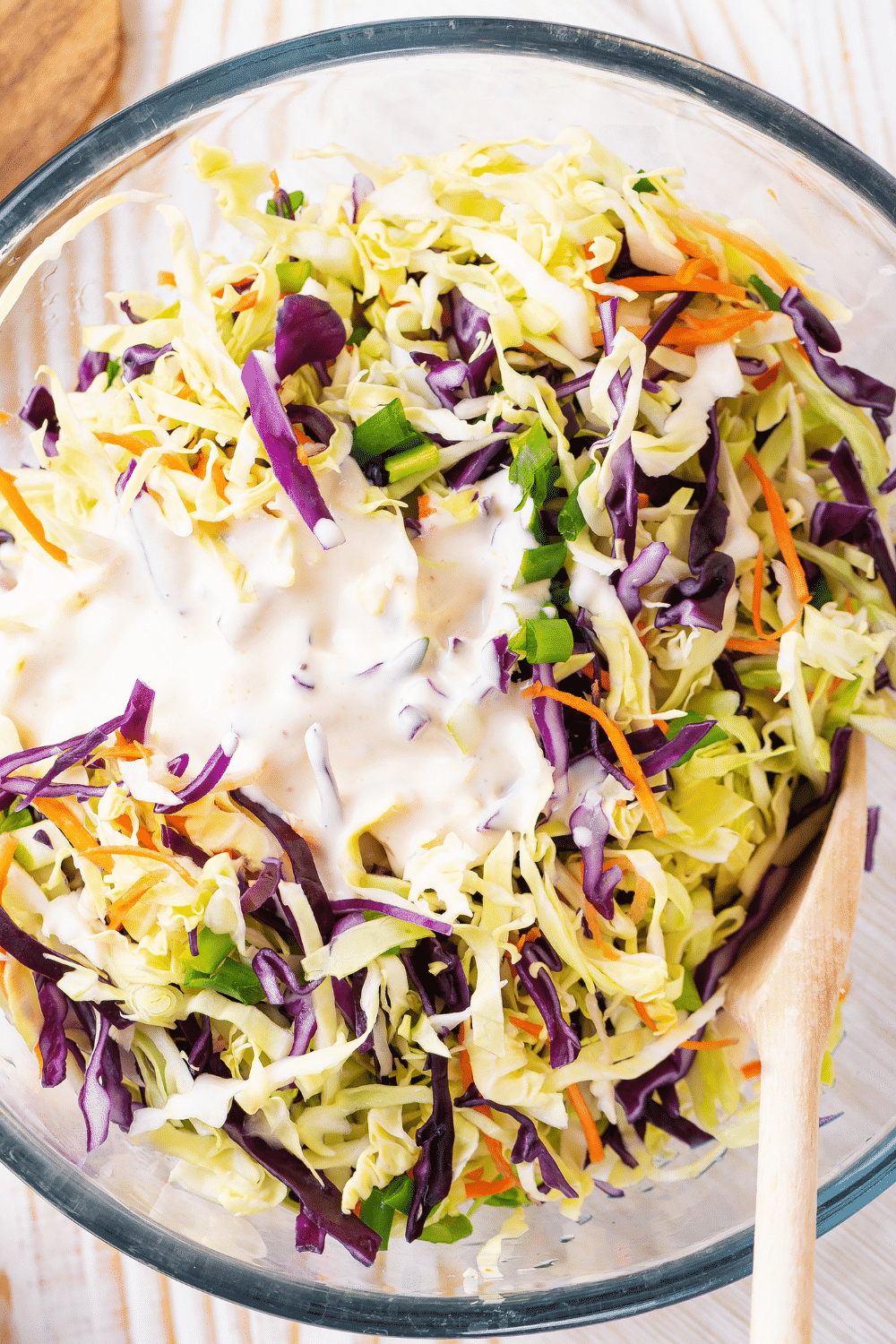 A glass bowl filled with coleslaw mix with coleslaw dressing on top.